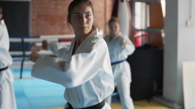 Medium shot of young female trainer wearing kimono teaching beginners in judo center