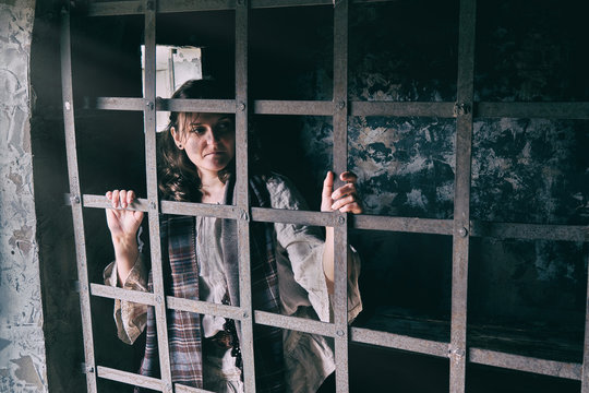 Young brunette woman in vintage clothes behind prison bars, copy space for text