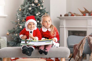 Cute little children in Santa costumes and with book at home on Christmas eve