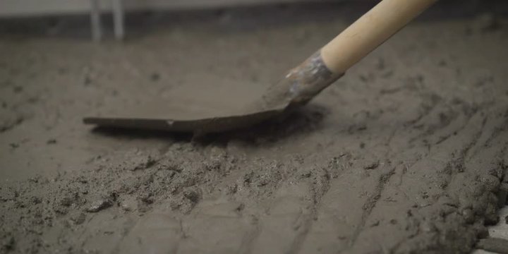 the solution is applied to the floor. Leveling the floor with a solution. The worker throws the solution with a shovel. A shovel settles the mortar on the concrete floor.