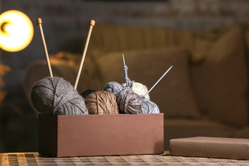Naklejka premium Box with knitting yarn and needles on table in room
