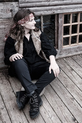 A young woman pirate sits cross legged on a wooden plank floor ship