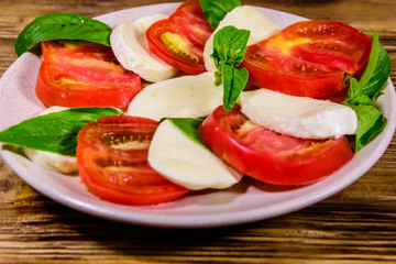 Plate with caprese salad (italian salad with cherry tomatoes, mozzarella cheese and basil leaves) on wooden table