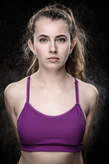 A young girl in a workout sports bra standing with her hand behind her back