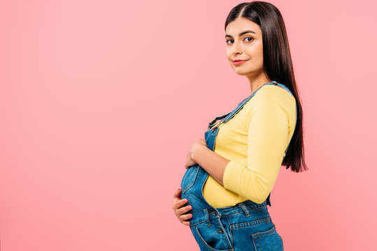 side view of pregnant pretty girl touching belly isolated on pink