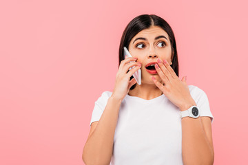 shocked pretty brunette girl talking on smartphone isolated on pink