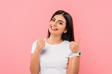 happy pretty brunette girl showing thumbs up isolated on pink