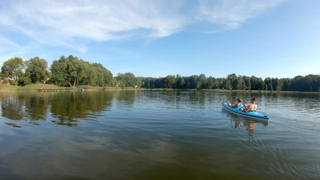 Two kayakers paddling on a peaceful lake during the day in a blue kayak. Aerial tracking shot at low altitude.