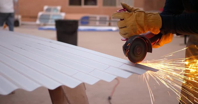 A construction worker using a power tool angle grinder to cut metal and send glowing bright sparks flying in slow motion.