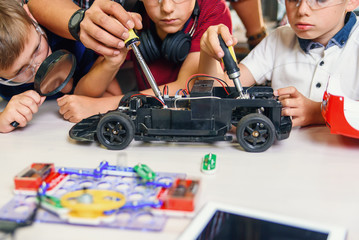 Male electronic engineer with european school children working in smart school lab and testing model of radio controlled electric car.