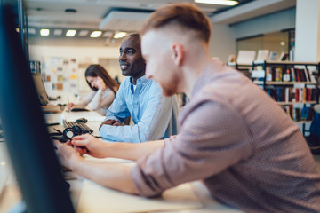 Black student sitting at computer table near classmate