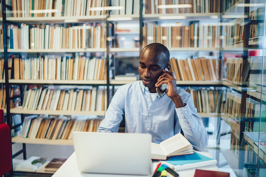 Serious ethnic student talking on smartphone near laptop in library - Powered by Adobe