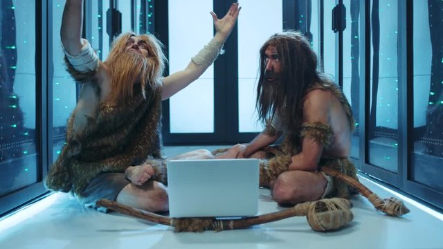 Tribe of prehistoric wild people sitting inside server cabinet, discovering modern technology, using a laptop computer. Funny cavemen in data center. Human evolution.