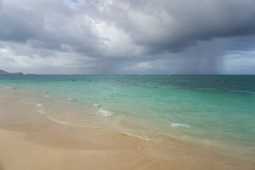 Fototapeta na wymiar Sunny tropical beach with overcast sky and rain in the distance