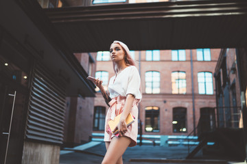 Stylish woman with smartphone in yard of administrative building