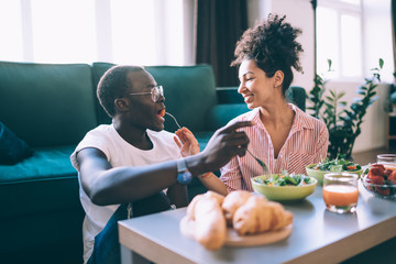 Multiracial couple eating salad while having romantic dinner at home