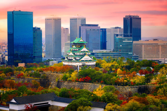 Osaka castle at the season change of autumn with the modern city urban building present in background at sunrise scenery