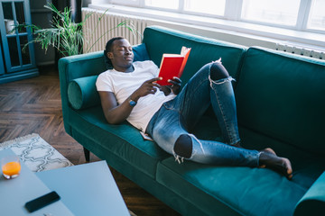Male relaxing on green sofa with book