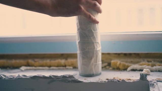 CU: skilled young builder applies spray foam insulation on stone windowsill from bottle in light spacious room closeup
