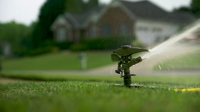 Lawn sprinkler going off over grass, suburban neighborhood, spring or summertime.