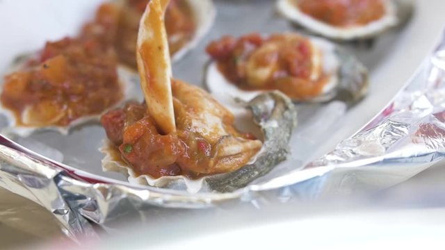 An oyster covered in spicy tomato sauce is placed back onto its shell in a beautiful delicious serving.