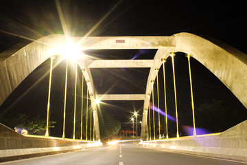 Fototapeta premium Illuminated bridge over the Rio Preto at night, located in the São José do Rio Preto municipal reservoir park, showcasing a stunning blend of urban architecture and nature