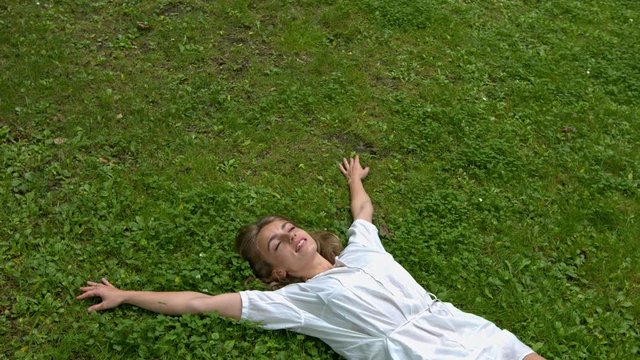 A young woman wearing a white dress laying down on the soft grass with her arms outstretched
