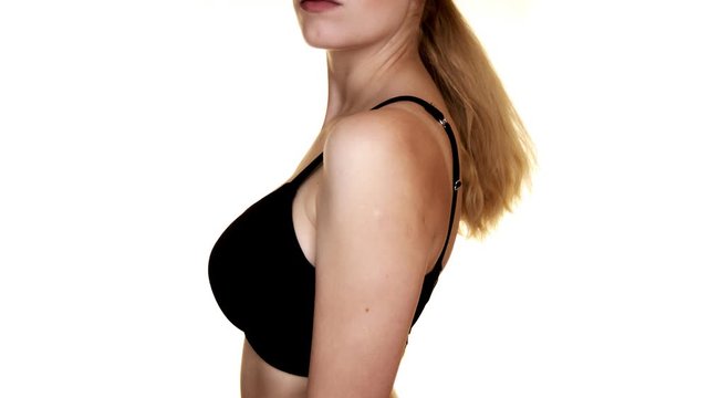 Close-up of a woman's torso with big breasts in a black bra. Shot in a studio on a white background.