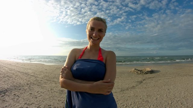 A woman with short blonde hair drying off after taking a swim at the beach, smiling and laughing at the camera