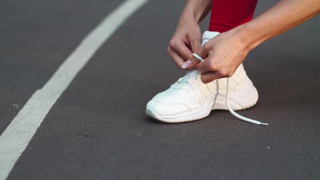 Closeup woman lacing up sneakers on track. Fitness girl lacing up shoes