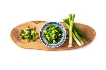 chopped spring onion, scallions, in a blue dish on wood board in white background