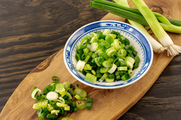 Chopped spring onion, scallion on wood board and wood background.