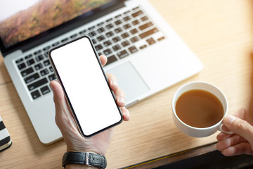 Mockup image blank white screen cell phone.men hand holding texting using mobile on desk at coffee shop.background empty space for advertise text.people contact marketing business and technology 