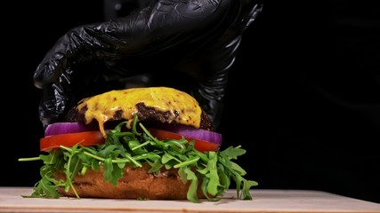 Craft burger is cooking on black background. Consist: sauce, arugula, tomato, red onion, bacon, red...