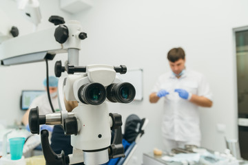 Doctor used microscope. Dentist is treating patient in modern dental office. Operation is carried out using cofferdam. Client is inserted and restored teeth, make denture. Orthodontist and assistant