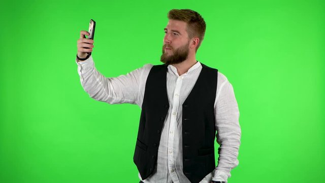 Man makes selfie on mobile phone then looking photos on green screen