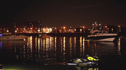 Fototapeta na wymiar Luxurious modern private yacht and boat at the pier at night. Ship crossing skyline in the harbor in summer awesome nightly. Colorful lights of city glow shine reflected in water wave at nighttime.