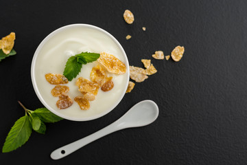 Yogurt in a white cup with a healthy breakfast cereal, placed on a black stone slab