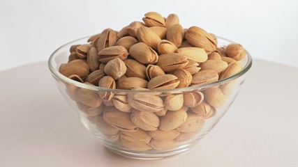 Nuts pistache rotate are on a table in a plate. Snack in transparent dish on an isolated white background are spinning moving. Delicious and healthy protein-rich diet food.