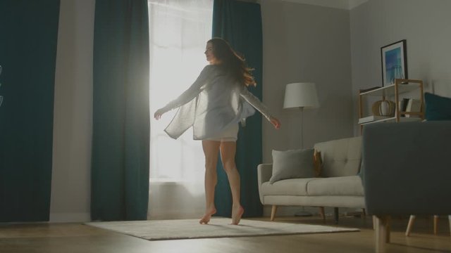 Beautiful Young Brunette Opens Curtains To let Morning Sunlight Illuminate Her Cozy Apartment, She Proceeds Dancing Beautifully and Quite Professionally across Room. Slow Motion Low Angle Side View