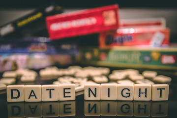 Date Night spelled out in letter tiles on black background with boardgames in the background