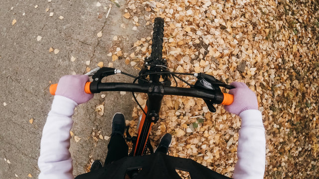 Pov View. One Caucasian Children Rides Bike Road In Autumn Park. Little Girl Riding Black Orange Mtb Cycle In Forest. Kid Goes Do Bicycle Sports. Biker Motion Ride With Backpack And Helmet.