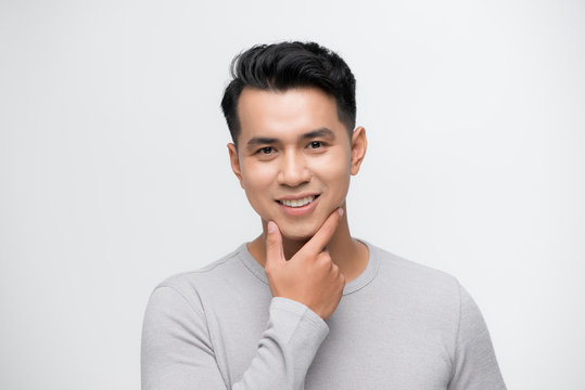 Happy smiling young handsome Asian man face with hand touching chin studio shot isolated