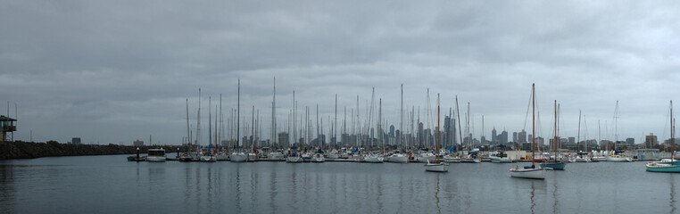 panoramic view of leisure boats tyed up in a rocky bay at St Kilda pier with the Melbourne city skyline stretching across the background in the late afternoon, Australia