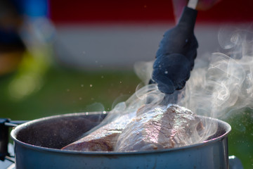 Juicy Angus steak frying in iron cast pan with smoke and Tongs on blurred nature background , cooking party picnic outdoor camping .