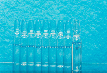 Glass medical ampoule vial for injection. Medicine is liquid sodium chloride with of aqueous solution in ampulla. Close up. Bottles ampule multicolor on background color and water. Human plasma.
