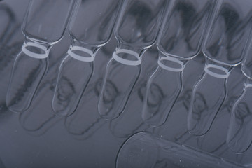 Glass medical ampoule vial for injection. Medicine is liquid sodium chloride with of aqueous solution in ampulla. Close up. Bottles ampule multicolor on background color and water. Human plasma.