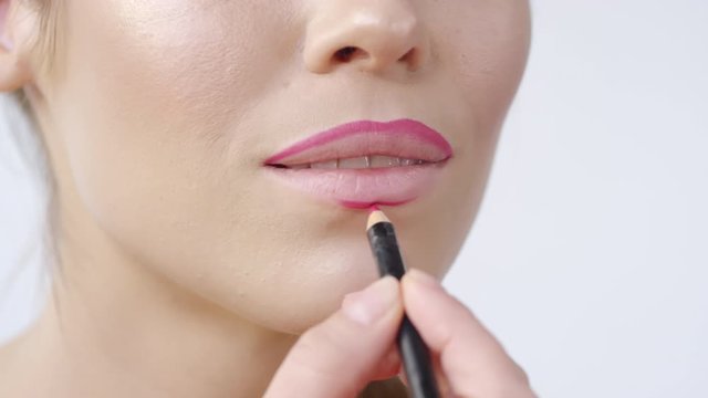 Extreme close up shot of unrecognizable woman applying pink lip liner before putting on lipstick