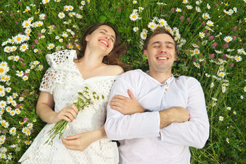 Happy couple lie in a camomile flower.