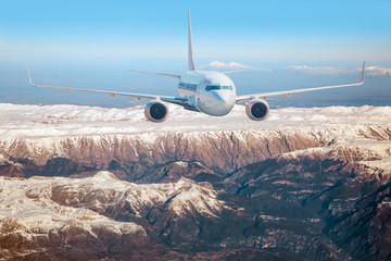 Airplane is flying over low clouds and snowy mountains